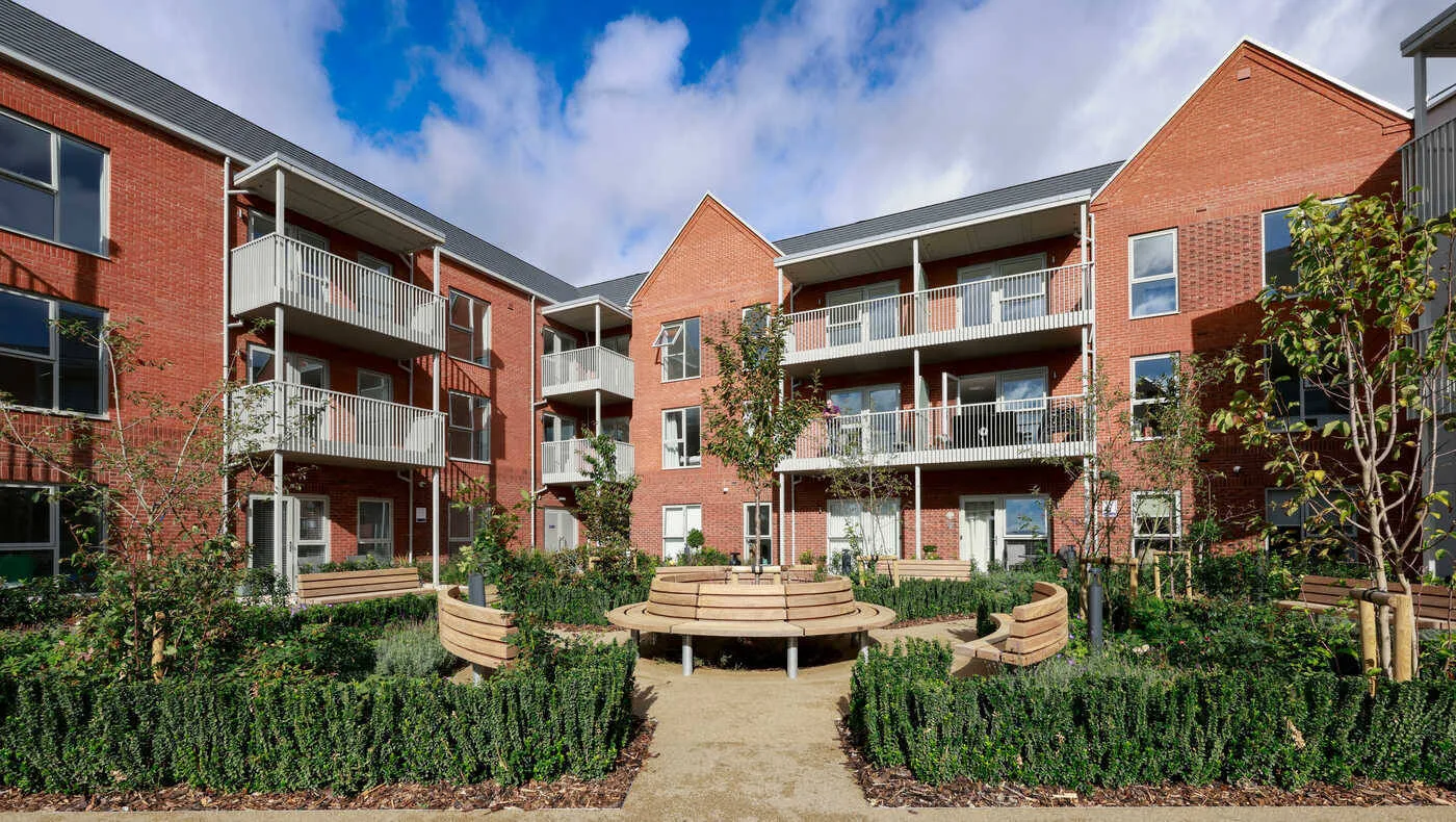 The landscaped inner courtyard of Blossom House in Edwalton, with a circular wooden bench, hedged beds and three-storey red brick flats with balconies on three sides.
