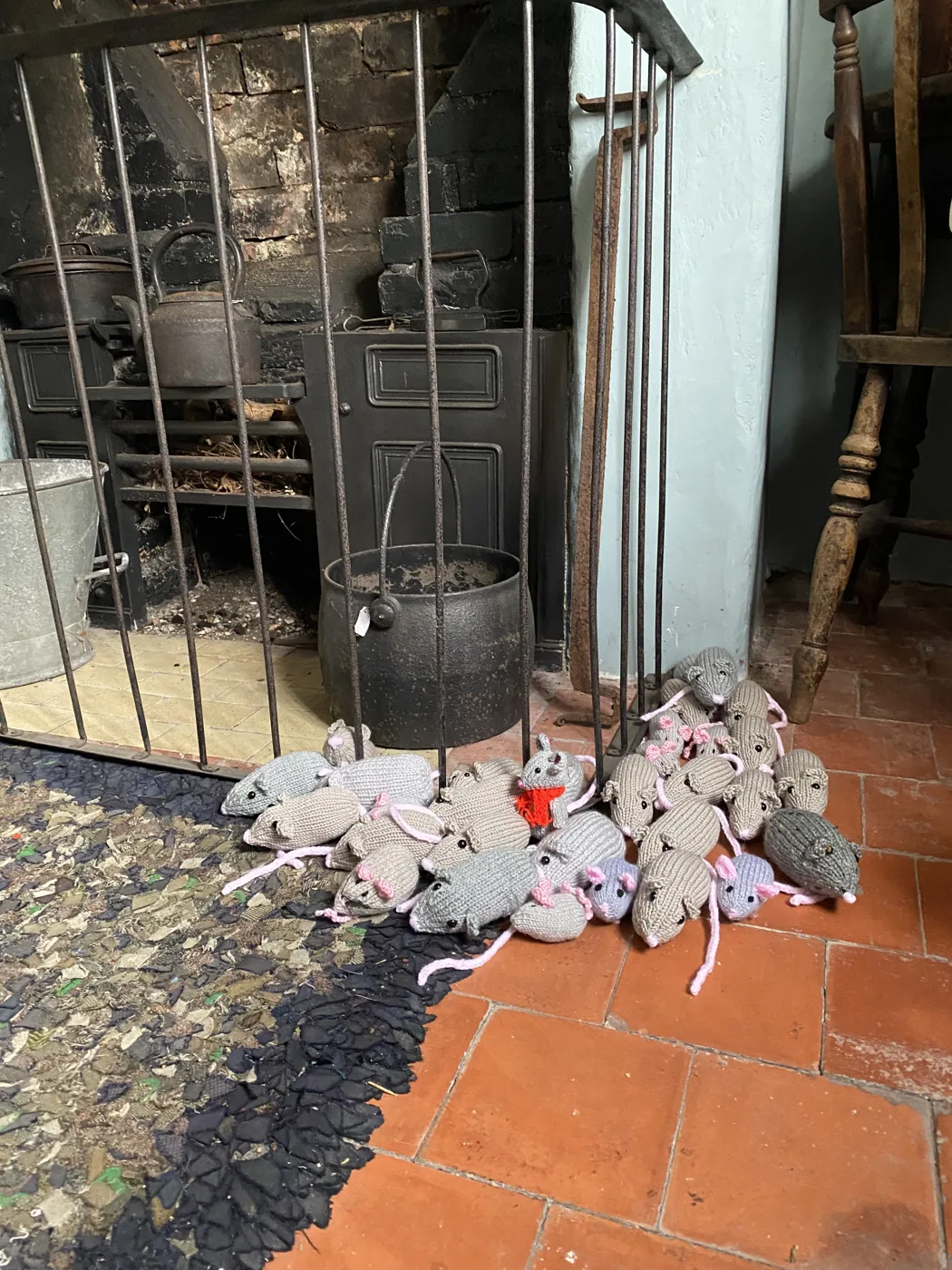 A pile of small knitted mice on the floor in front of a cottage range