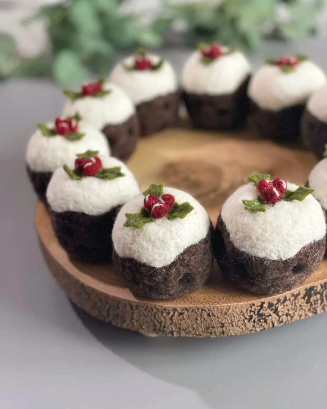 A ring of needle-felted Christmas puddings with white tops and red berries on a wooden board