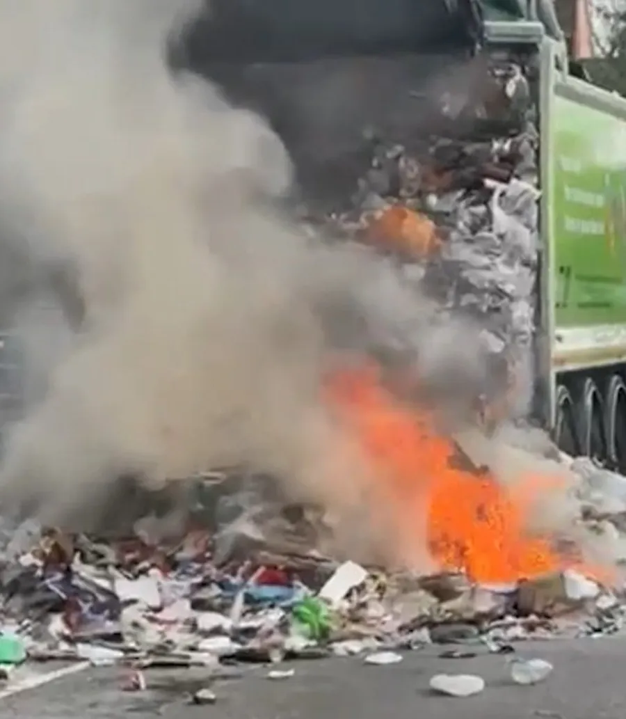 Smoke and flames rising from a pile of waste tipped out of the back of a green Rushcliffe bin lorry onto the road